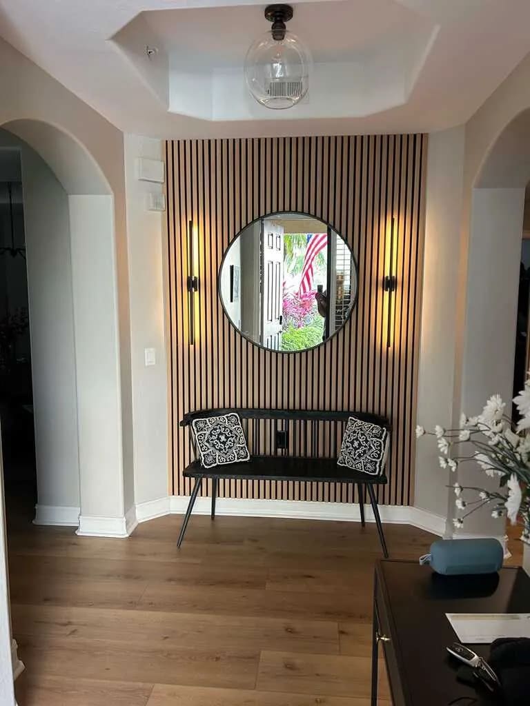Entryway accent wall with vertical wood slats, a round black mirror between two linear sconces, and wide-plank flooring