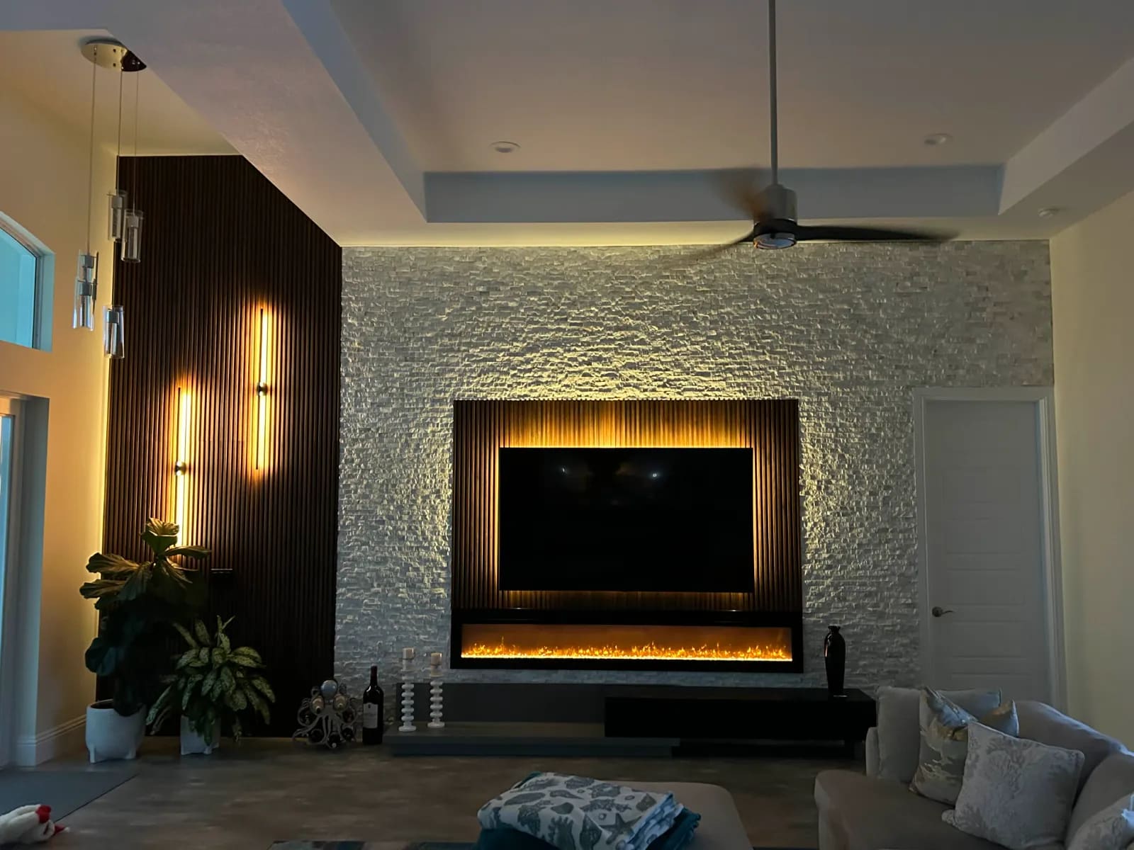 Living room entertainment wall in white stacked stone with a backlit wood-slat TV surround, linear fireplace and slatted accent panel