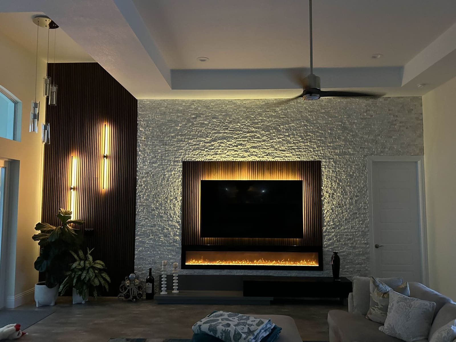 Living room feature wall in white stacked stone with a backlit TV over a linear fireplace and dark wood slat panels